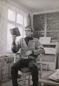Gråtone foto av ung mann (Frode Kayser) som sitter i en stol og leser høyt